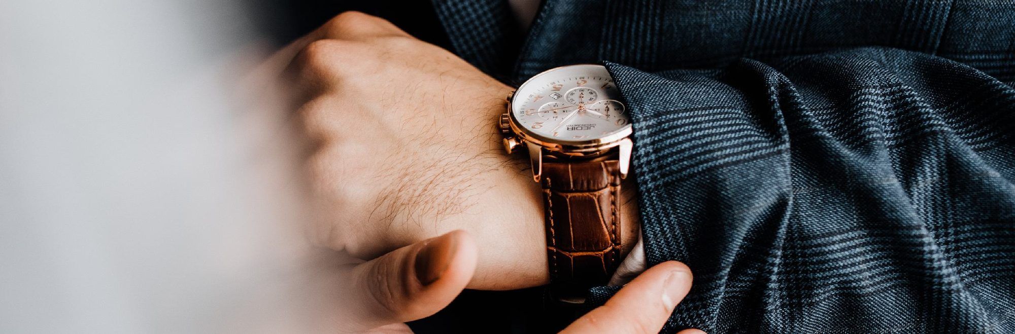 Hand an einer Armbanduhr mit Lederarmband am Handgelenk eines Mannes im Sakko