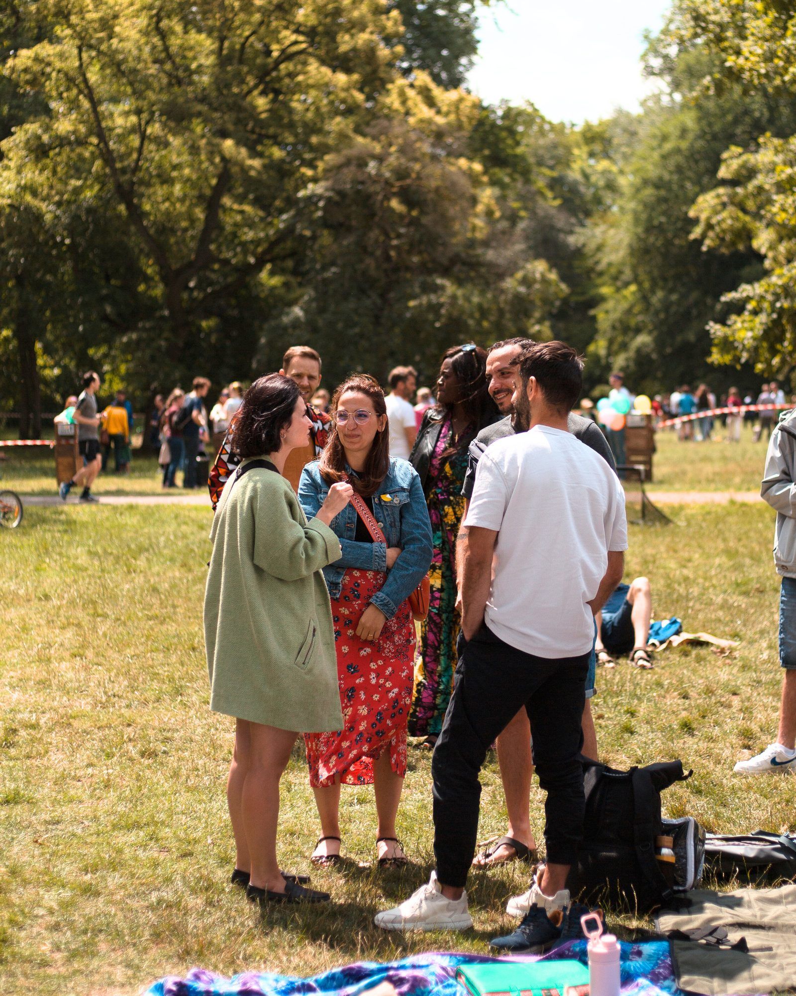 Eine Gruppe von Menschen steht im Sommer auf einer Wiese in einem Park und unterhält sich