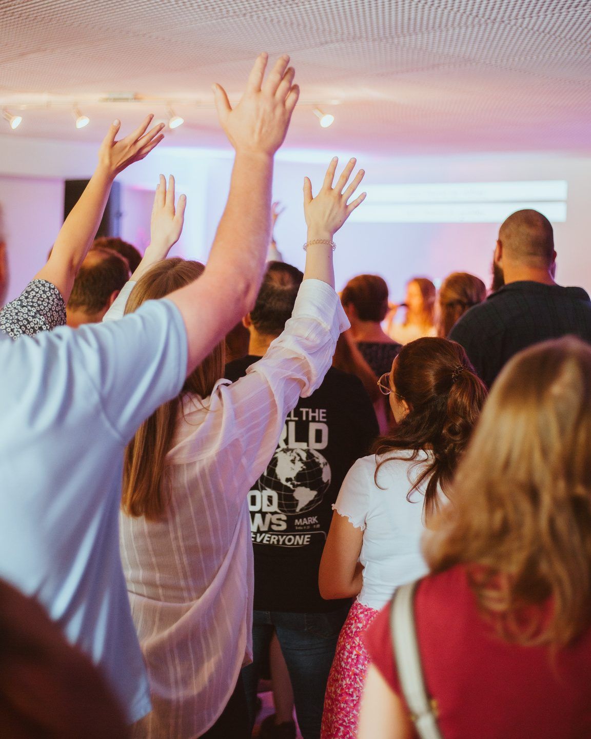 Menschen im Gottesdienst heben die Hände, vorne eine Sängerin auf einer Bühne in violettem Licht