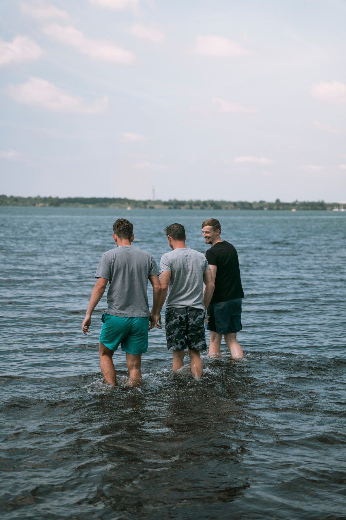 Drei Männer waten von hinten gesehen in einen See