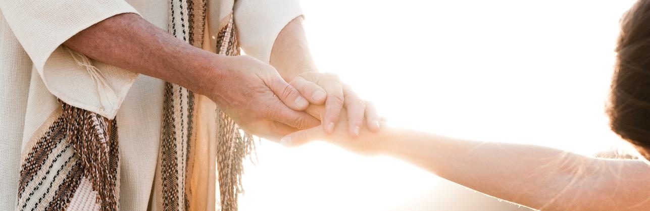 Eine Hand in einem gestreiften Gewand greift im hellen Gegenlicht nach einer ausgestreckten Hand