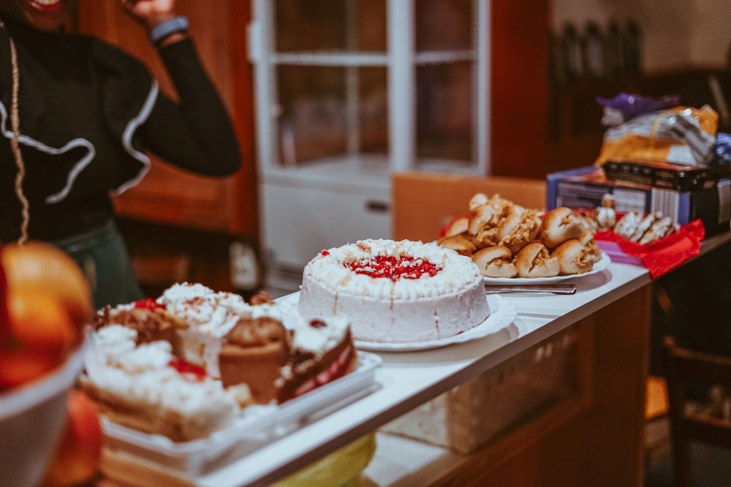 A table full of cakes and pastries, with a woman standing next to it