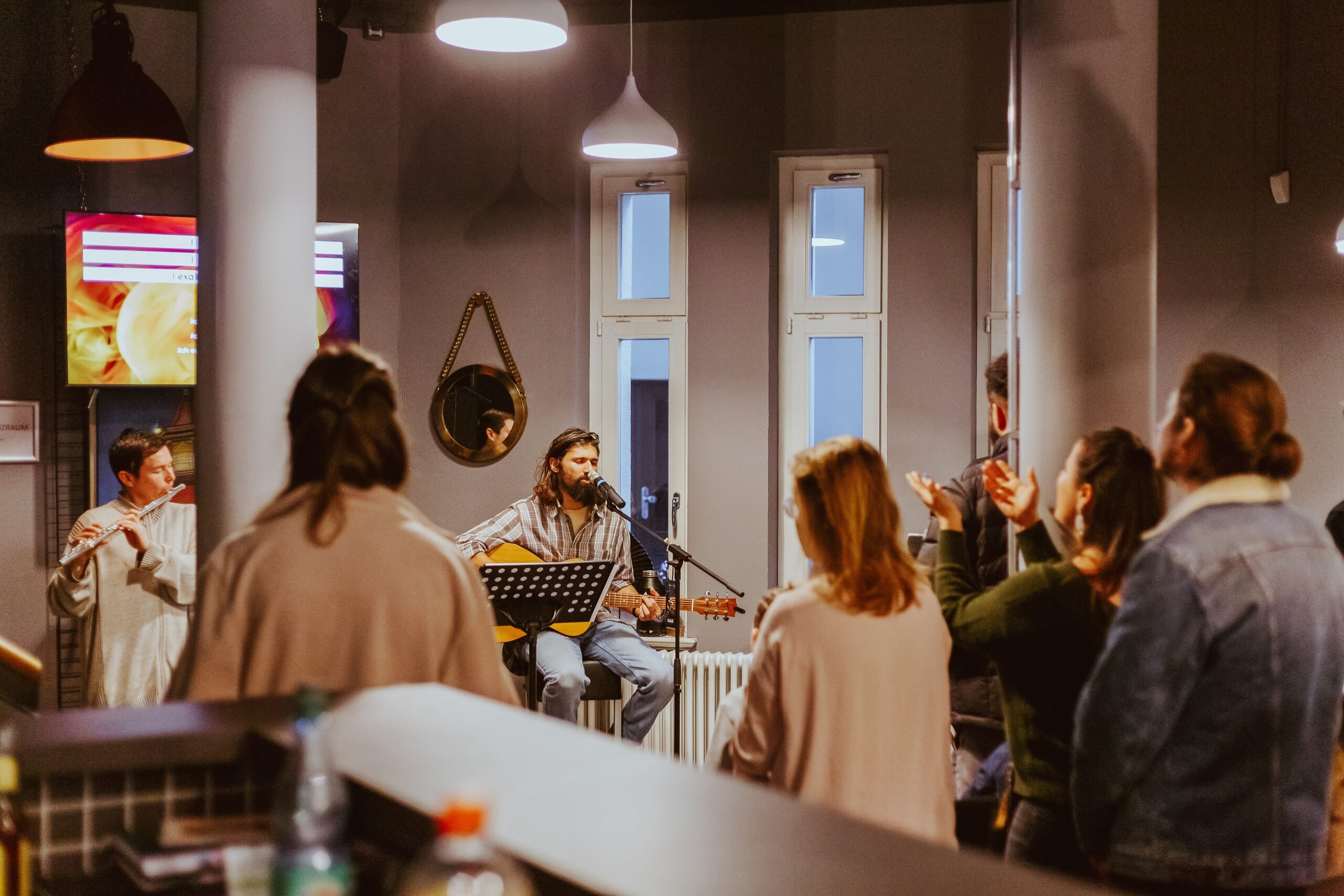 Musicians with guitar and flute leading worship while people clap along