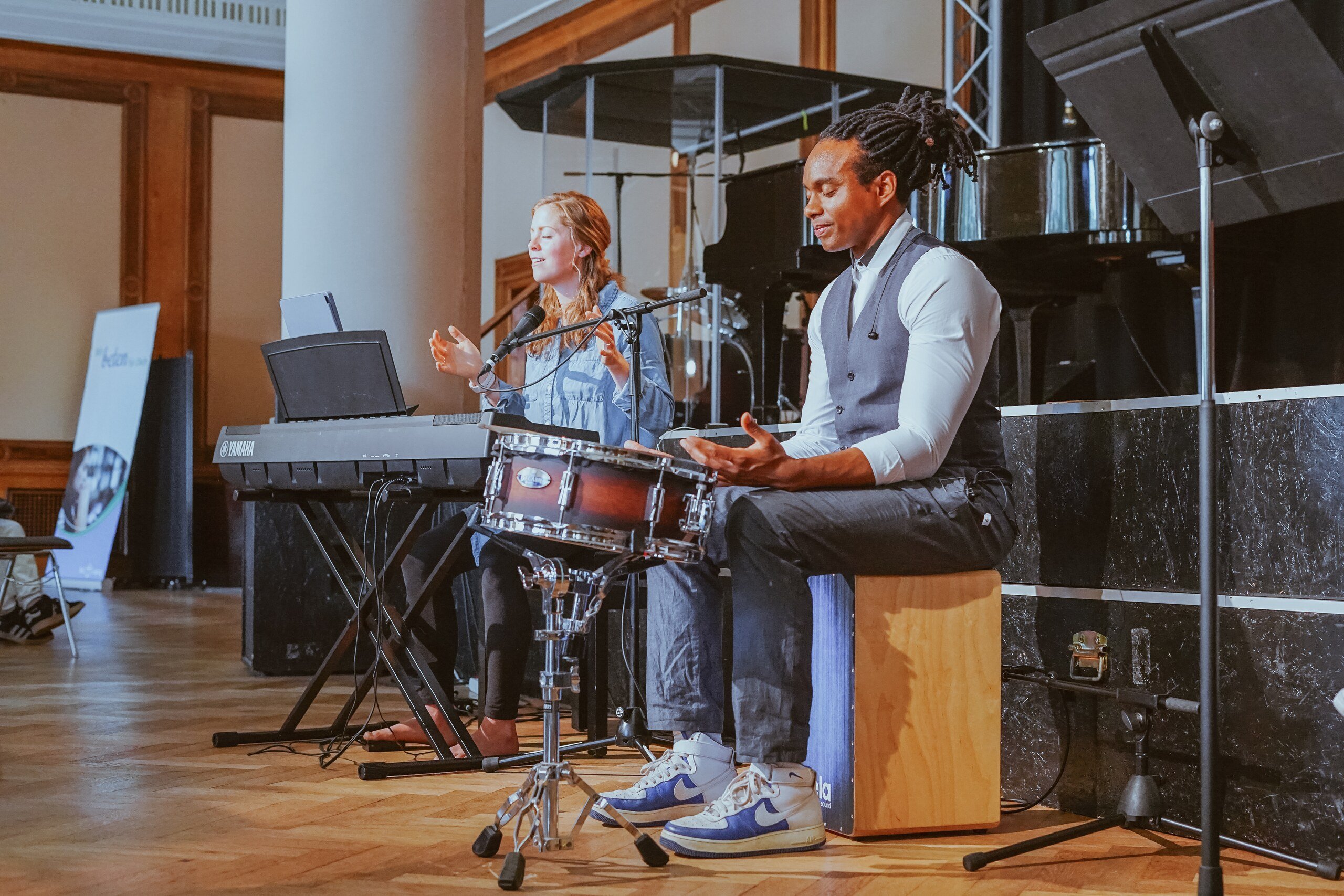 A woman singing and a man playing drums and cajón in the worship team